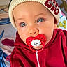 baby, child, pacifier, blue_eyes, beanie, hat, red_hoodie, clothing, face, portrait, indoor, cute, infant, person, expression, closeup, colorful_background, pattern, soft_lighting, young