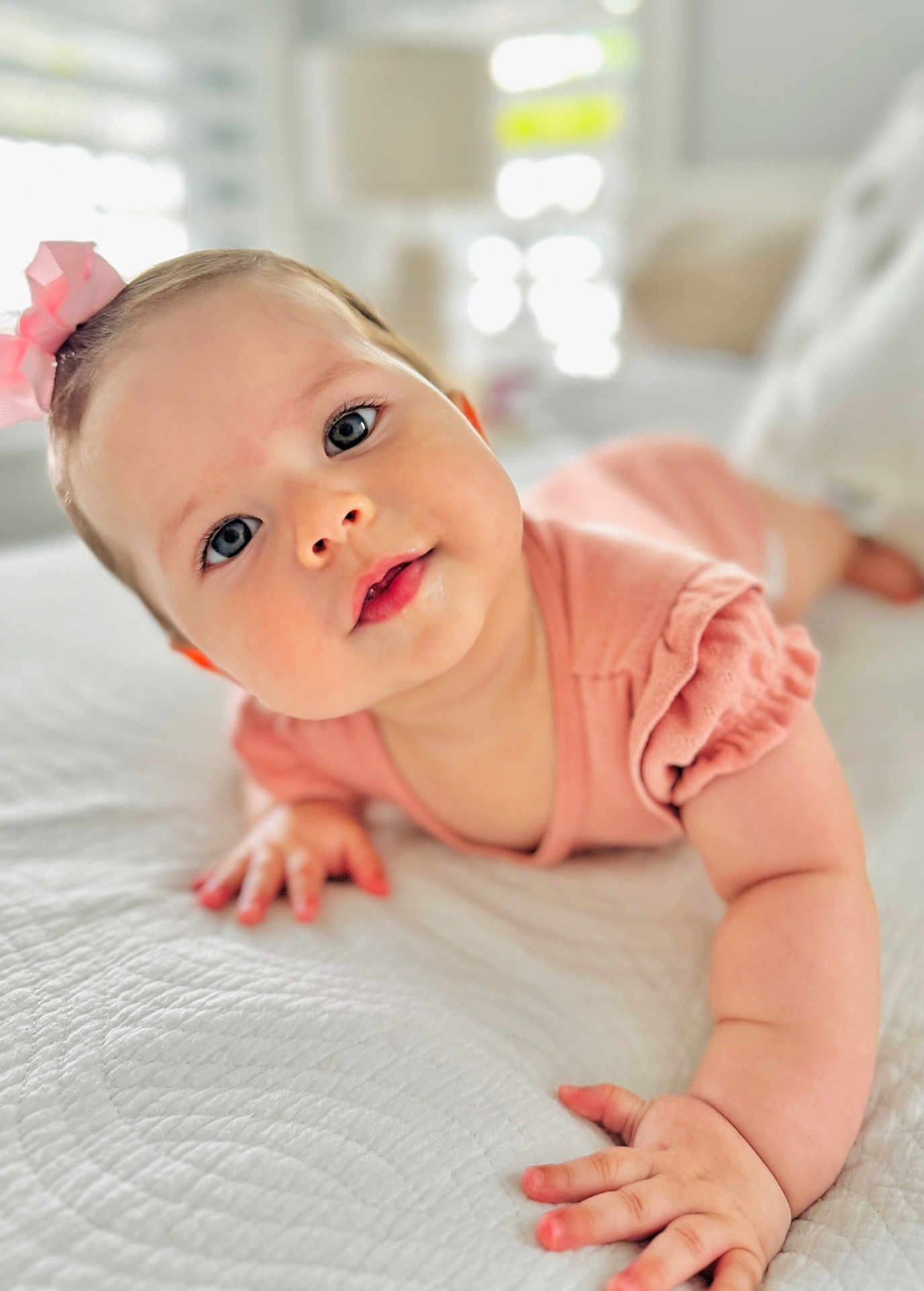 Luciana is registered to the contest to win money with this photo: baby, infant, child, pink_bow, blue_eyes, crawling, bed, white_bedspread, soft_texture, natural_light, curious_expression, close_up, portrait, indoor, cute, small_hands, sleepwear, toddler, headband, skin