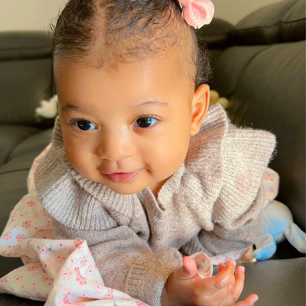 Noblesse Maelys a rejoint le concours — aidez-le/la à gagner de superbes lots ! adorable, baby, blanket, child, couch, cozy, cute, face, hair_bow, hand, happy, indoor, infant, knitted_sweater, person, pink, portrait, skin, smile, young_child