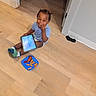 child, toddler, smile, tablet, floor, food, snack, plate, socks, hair, doorway, indoors, wooden_floor, technology, happy, casual, playing, person, clothing, fun