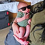 baby, infant, sunglasses, green_onesie, person, holding, arm, hand, indoor, table, stroller, foot, skin, casual, relaxed, cool, tiny, adult, background, blur