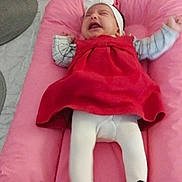 Beatriz Amaro participe au concours pour gagner de l'argent avec cette photo : baby, infant, crying, pink_cushion, red_dress, white_tights, headband, indoor, flooring, shoes, footwear, child, person, expression, furniture, soft_surface, home, clothing, cute, upset
