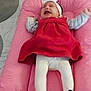 baby, infant, crying, pink_cushion, red_dress, white_tights, headband, indoor, flooring, shoes, footwear, child, person, expression, furniture, soft_surface, home, clothing, cute, upset