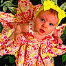baby, child, blue_eyes, yellow_bow, floral_dress, curious, portrait, closeup, colorful, patterned_clothing, headband, infant, cute, baby_girl, looking_up, vibrant_colors, indoor, soft_lighting, person, face