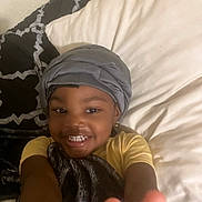 Dazani joined the competition — help win amazing prizes! child, smiling, peace_sign, blanket, head_wrap, bed, pillow, yellow_shirt, happy, indoor, portrait, person, young_child, cozy, casual, comfort, relaxed, home, cute, gesture