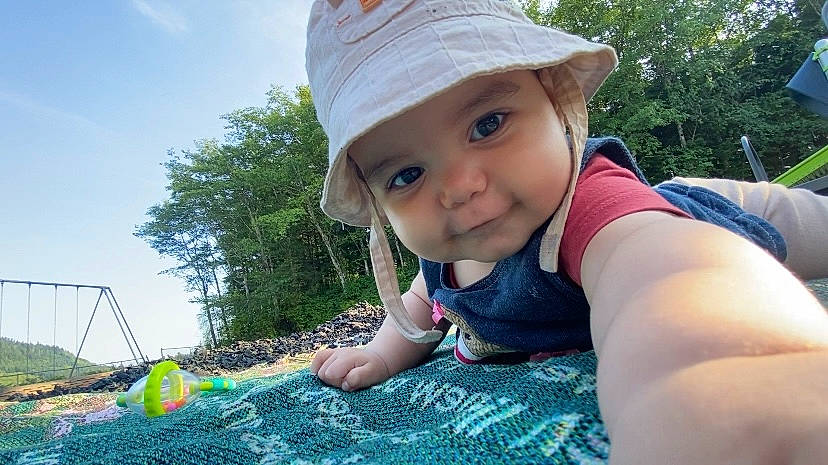 Amelia joined the competition — help win amazing prizes! baby, blanket, blue_sky, bucket_hat, candid, child, close_up, daylight, expression, grass, infant, nature, outdoor, playful, portrait, reaching, smiling, sunny, swing_set, trees