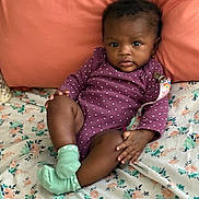 Mulani is registered to the contest to win money with this photo: baby, infant, child, onesie, purple_clothing, polka_dot, socks, mint_green, bed, bedspread, floral_pattern, pillow, coral_color, skin, face, eyes, hands, legs, indoor, portrait