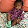 baby, infant, child, onesie, purple_clothing, polka_dot, socks, mint_green, bed, bedspread, floral_pattern, pillow, coral_color, skin, face, eyes, hands, legs, indoor, portrait
