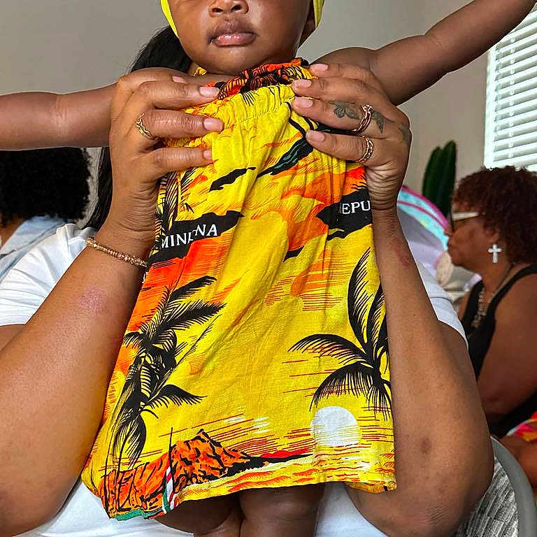 Mulani is registered to the contest to win money with this photo: adult_hands, baby, casual, child, dress, face, family, feet, hands, holding, indoor, orange, patterned_clothing, people, portrait, room, seated, toddler, window, yellow