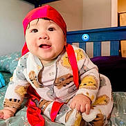 Matheo is registered to the contest to win money with this photo: animal_print, baby, bed, bedding, blanket, child, cute, eyes, face, foot, furniture, hand, indoors, infant, mouth, onesie, person, red_headscarf, smiling, soft