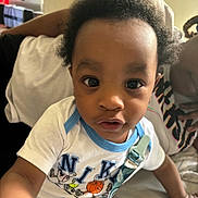 Dwane Jr. is registered to the contest to win money with this photo: adult, background, casual, child, closeup, clothing, couch, curly_hair, expression, face, furniture, home, indoor, nike, pacifier_clip, person, portrait, reaching, shirt, toddler