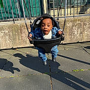 Dwane Jr. joined the competition — help win amazing prizes! toddler, child, swing, playground, denim_jacket, jeans, cap, smile, outdoor, sunlight, shadow, rubber_matting, metal_fence, green_door, urban, happy, baby_swing, person, clothing, play