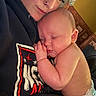 adult, affection, baby, caregiver, chair, child, close_up, cozy, cuddling, diaper, face, family, indoor, infant, nap, portrait, shirt, sleeping, sleepy, warm_lighting