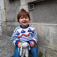 Robin participe au concours pour gagner de l'argent avec cette photo : toddler, child, smiling, sweater, toy, stuffed_animal, jeans, white_shoes, outdoor, stone_step, wall, red_hair, cute, happy, casual_clothing, playful, young_child, sitting, daylight, urban