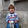 toddler, child, smiling, sweater, toy, stuffed_animal, jeans, white_shoes, outdoor, stone_step, wall, red_hair, cute, happy, casual_clothing, playful, young_child, sitting, daylight, urban