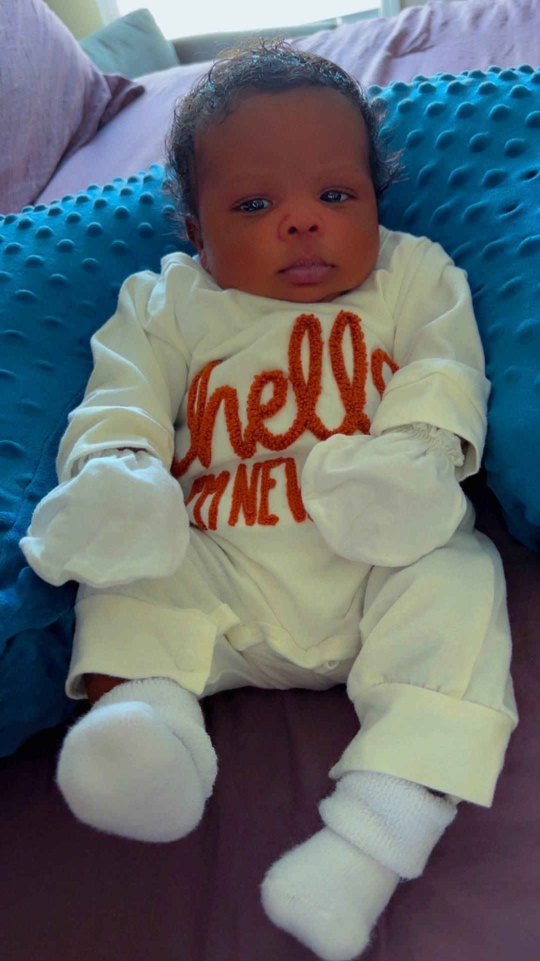 Isaiah joined the competition — help win amazing prizes! baby, blue_pillow, child, comfort, cozy, curly_hair, cute, face, home, indoors, infant, looking, lying_down, mittens, newborn, portrait, resting, socks, soft_fabric, white_clothing