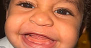 Aziel joined the competition — help win amazing prizes! baby, toddler, smile, happy, face, curly_hair, bib, dinosaur_pattern, child, portrait, cute, teeth, skin, eyes, indoors, closeup, person, infant, joy, expression