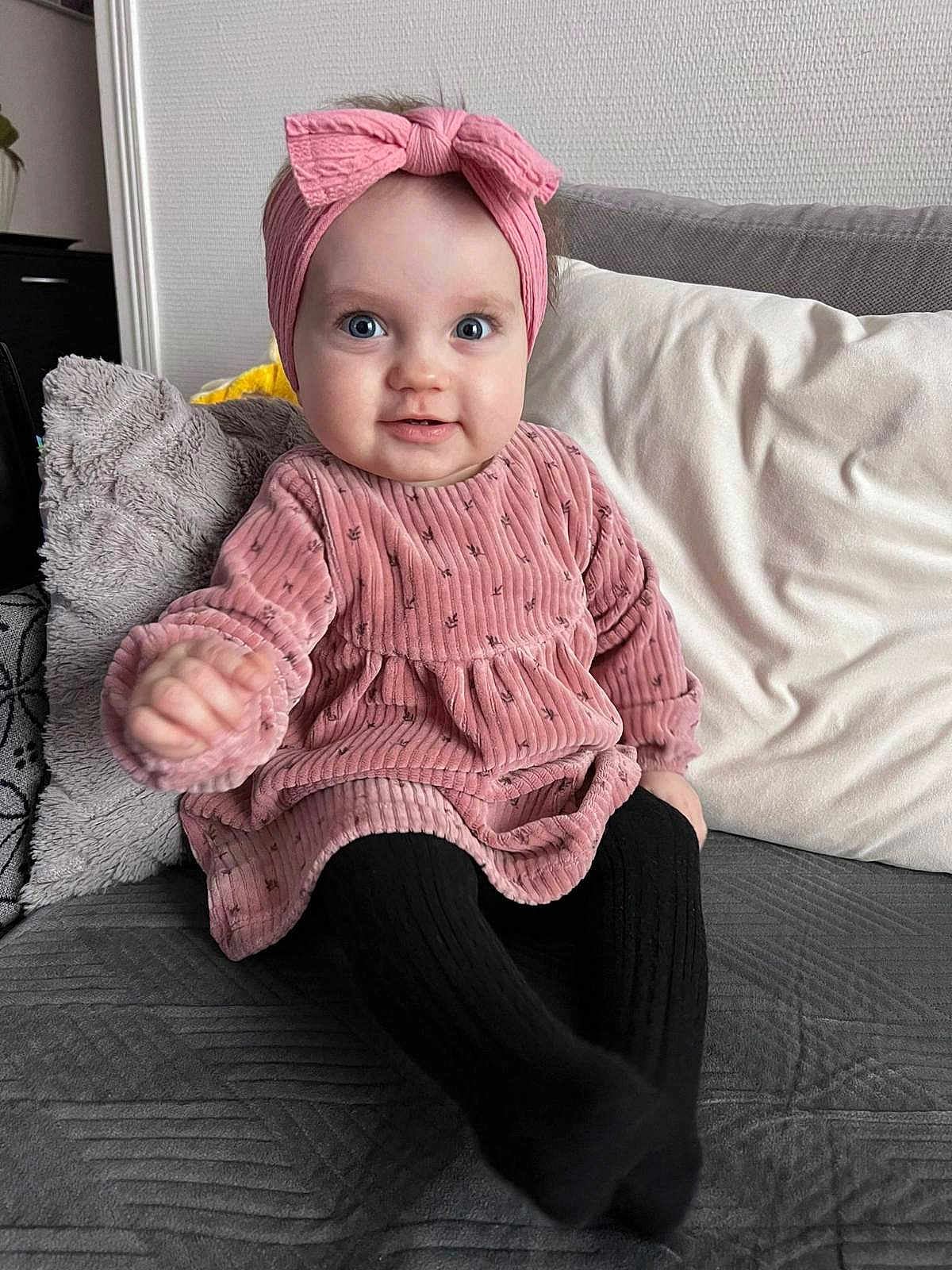 Jana participe au concours pour gagner de l'argent avec cette photo : baby, child, pink_dress, headband, bow, couch, pillow, black_tights, smile, happy, indoor, portrait, sitting, cute, infant, cozy, childrens_clothing, home, furniture, person
