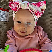 Rowyn is registered to the contest to win money with this photo: baby, infant, headband, bow, pink_clothing, smile, face, toy, colorful, seat, baby_toys, portrait, cute, child, young, indoor, closeup, happy, soft_lighting, infant_girl