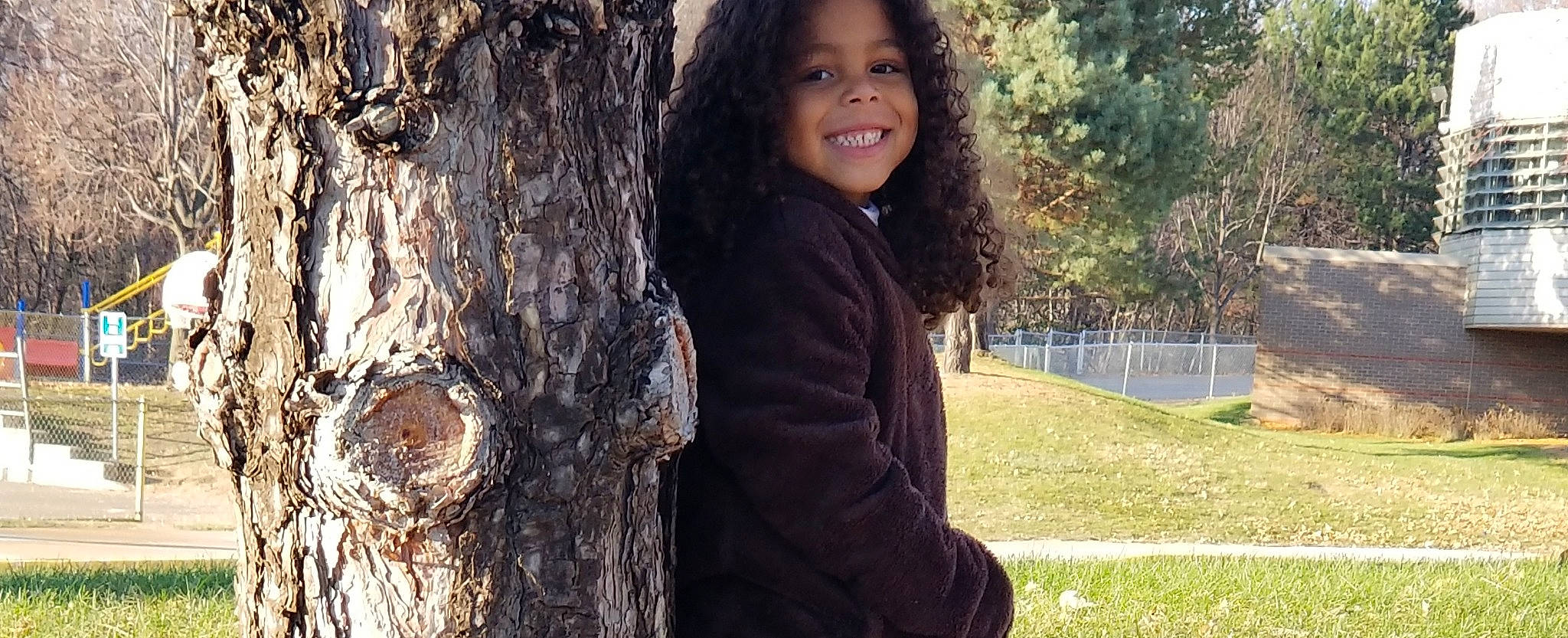 Deklyn is registered to the contest to win money with this photo: adaptation, black_hair, brown_hair, child, child_model, grass, hair, hairstyle, happy, joy, long_hair, person, photography, plant, smile, tree, trunk, woody_plant