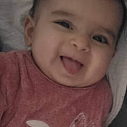 Giulia participe au concours pour gagner de l'argent avec cette photo : baby, infant, smiling, tongue_out, face, portrait, close_up, onesie, pink_clothing, bedding, blanket, chubby_cheeks, dark_hair, hand, ear, lying_down, cute, happy, bedroom, soft_lighting