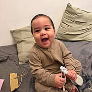 Ethan Chaparro is registered to the contest to win money with this photo: baby, bed, brush, child, comfort, cozy, cute, furniture, handheld_object, happy, indoors, infant, pajamas, person, pillow, playful, relaxed, room, sitting, smiling