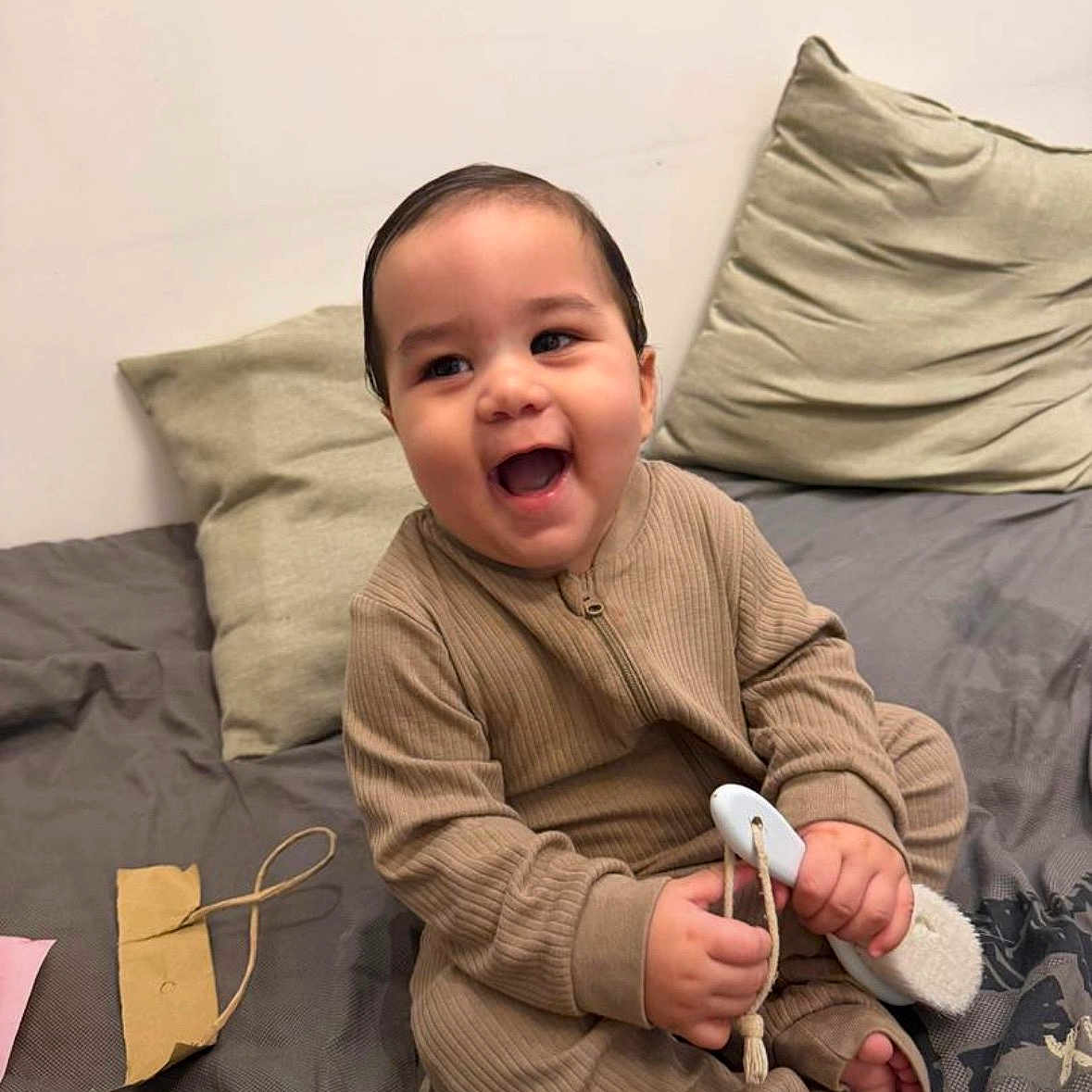 Ethan Chaparro is registered to the contest to win money with this photo: baby, bed, brush, child, comfort, cozy, cute, furniture, handheld_object, happy, indoors, infant, pajamas, person, pillow, playful, relaxed, room, sitting, smiling
