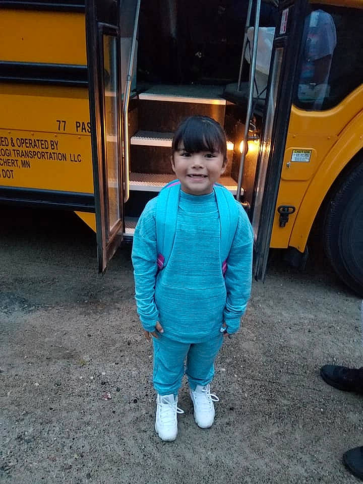 Tracy is registered to the contest to win money with this photo: asphalt, bus, car, child, commercial_vehicle, joy, mode_of_transport, outerwear, person, photography, smile, snapshot, standing, transport, vacation, vehicle, wheel, yellow