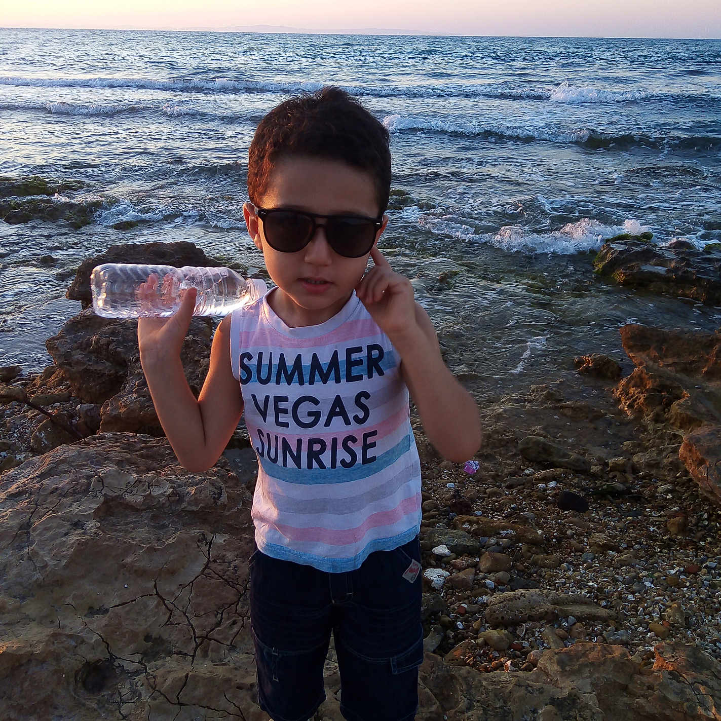 Sbei Youcef participe au concours pour gagner de l'argent avec cette photo : boy, casual_clothing, child, daylight, flip_flops, nature, outdoor, person, rocky_shore, sea, shoreline, shorts, sky, standing, summer, sunglasses, sunset, water, water_bottle, waves