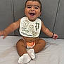 Guzey is registered to the contest to win money with this photo: baby, smiling, bib, diaper, socks, happy, infant, child, cute, cushion, gray_background, sitting, arm_movement, portrait, indoor, face, clothing, expression, cheerful, young_child