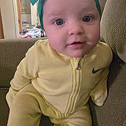 Loralie is registered to the contest to win money with this photo: adorable, baby, big_eyes, bow, child, close_up, couch, curious, face, headwrap, infant, living_room, messy_background, nike_logo, portrait, sitting, sofa, toys, yellow_onesie, zipper