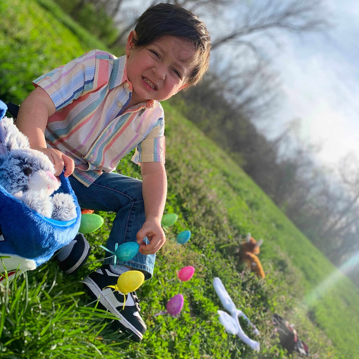 Melek joined the competition — help win amazing prizes! basket, boy, casual_clothing, child, colorful, daytime, easter_eggs, grass, greenery, happy, jeans, nature, outdoor, playful, plush_toy, smile, sneakers, spring, sunlight, trees