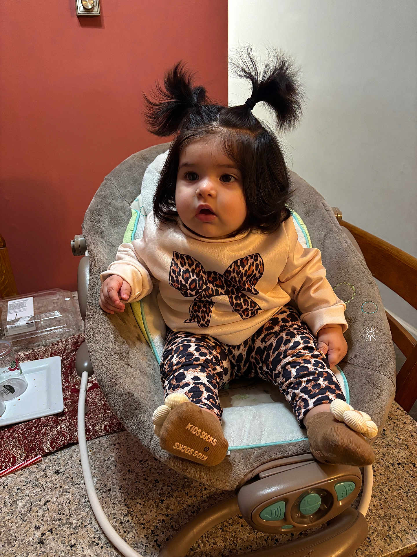 Ariana joined the competition — help win amazing prizes! baby, child, infant, pigtails, leopard_print, socks, baby_rocker, indoor, curious, clothing, table, countertop, chair, face, person, hair, cute, seated, expression, furniture