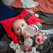 Kae-Lynn is registered to the contest to win money with this photo: baby, bottle, blanket, bed, pillow, clothing, face, person, indoor, toy, sleepwear, child, laying_down, feeding, cute, soft, comfort, red, patterned, cozy