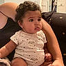 Kaliyah is registered to the contest to win money with this photo: baby, child, curly_hair, onesie, indoor, person, arm, hand, furniture, blanket, pacifier, cozy, curious, sitting, cute, infant, home, soft_lighting, relaxed, portrait