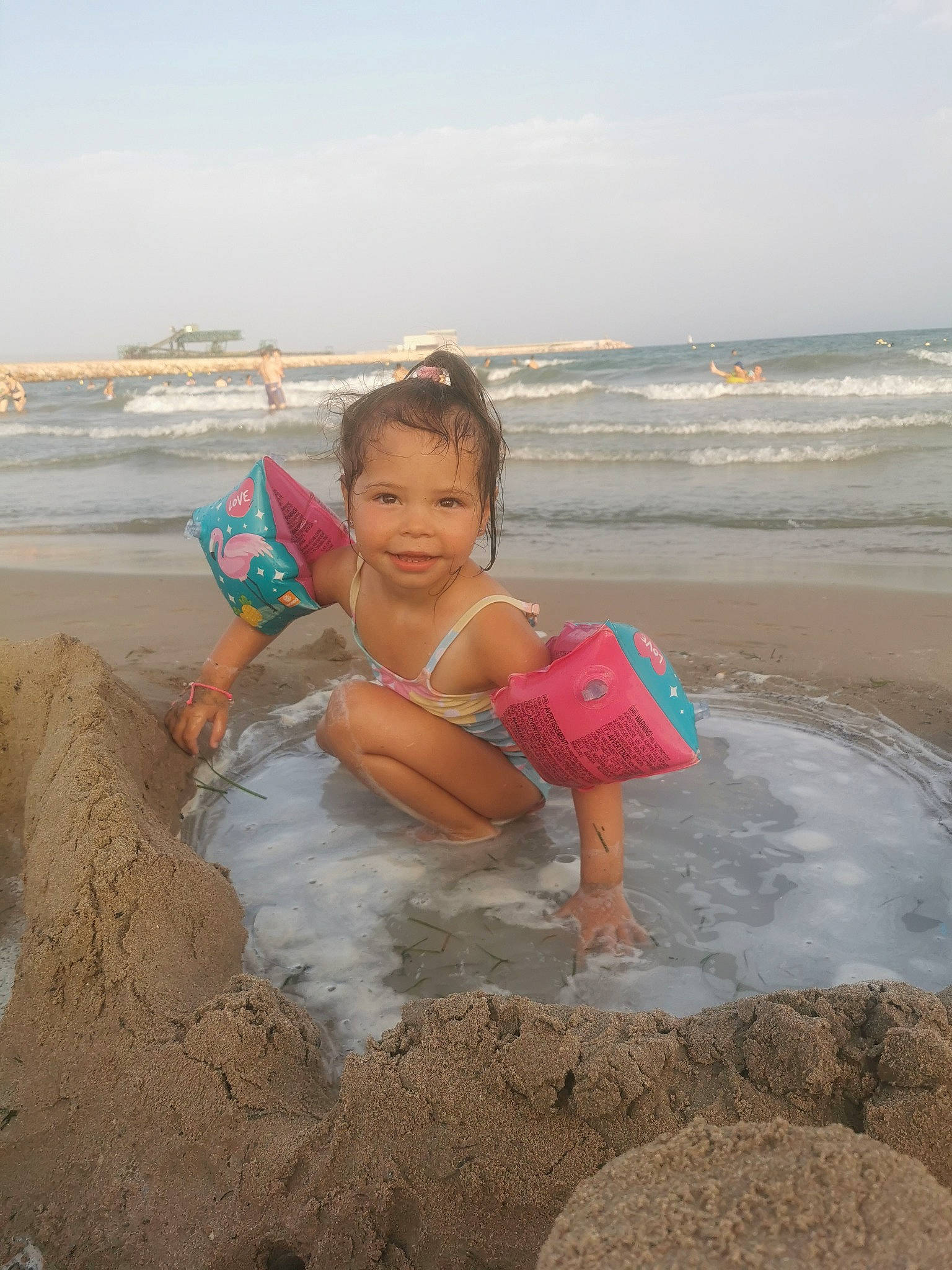 Lyia participe au concours pour gagner de l'argent avec cette photo : beach, body_of_water, cloud, fun, happy, hat, holiday, joy, leg, leisure, people_on_beach, person, sand, shorts, sitting, sky, smile, t_shirt, thigh, toddler