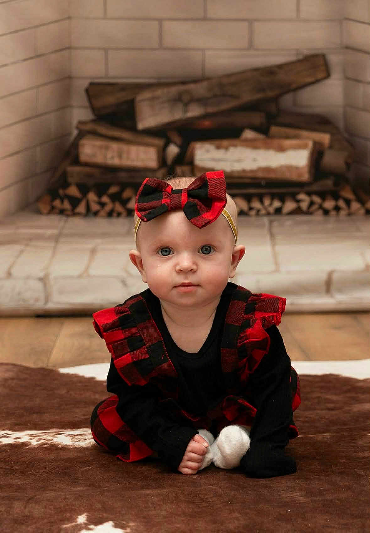 Elliana is registered to the contest to win money with this photo: baby, child, plaid, dress, headband, bow, fireplace, firewood, rug, floor, indoors, person, cute, sitting, portrait, blue_eyes, clothing, infant, home, cozy