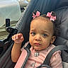 baby, baby_girl, blue_eyes, casual_clothing, child, closeup, curly_hair, cute, expression, indoor, infant, person, pink_bows, pink_shirt, portrait, seatbelt, sitting, stroller, toddler, young_child