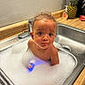 bath, bathing, bubble_bath, child, countertop, curly_hair, cute, expression, foam, indoor, kitchen, pineapple, playful, portrait, sink, small_person, soap, toddler, water, wet_skin