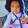 Harmony is registered to the contest to win money with this photo: baby, child, hat, polka_dot, bib, outdoor, person, hand, foot, curious, blue_eyes, clothing, sitting, chair, wooden_deck, adult_hand, sunhat, pink_pants, casual, portrait