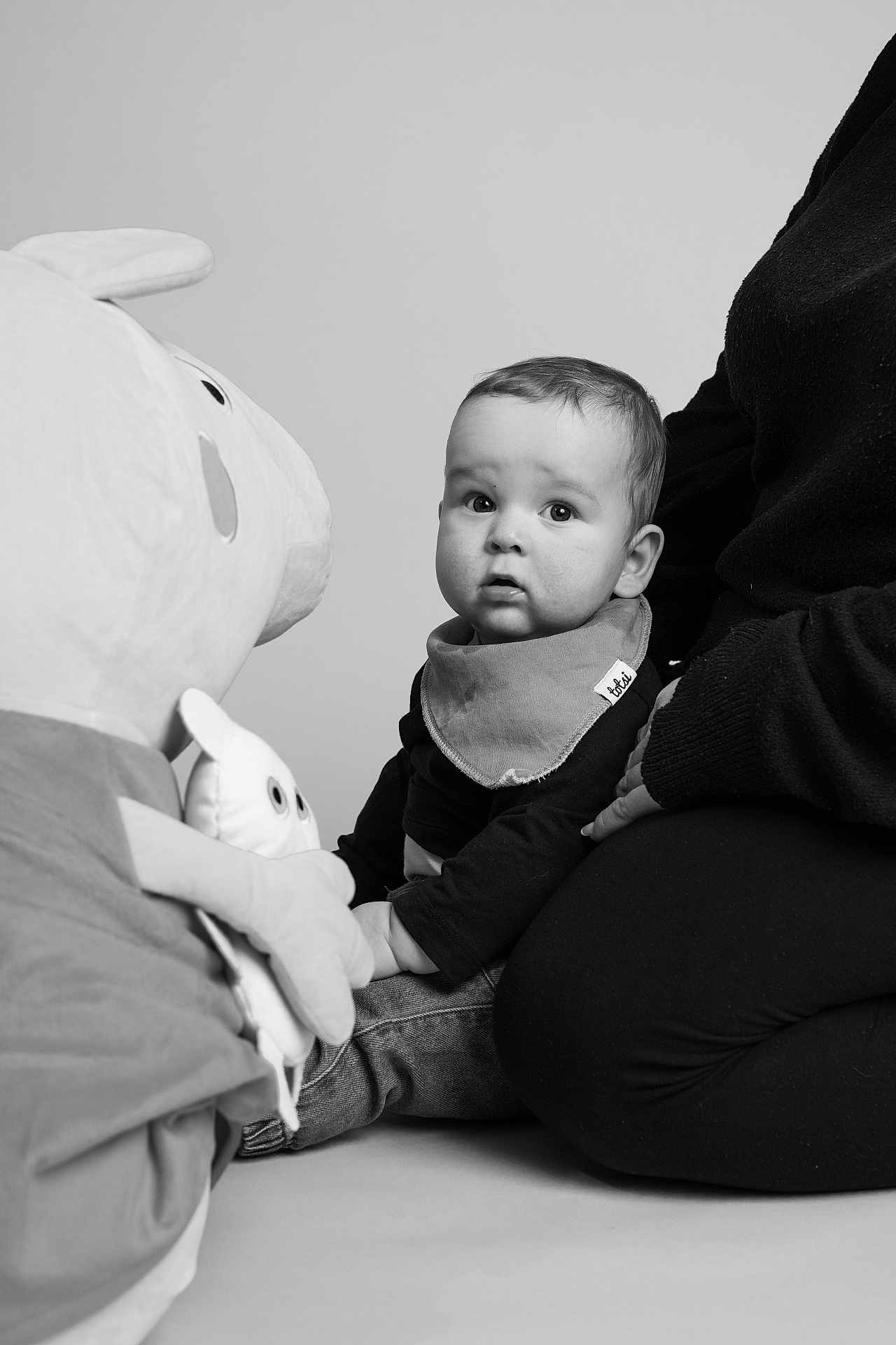 Teddy joined the competition — help win amazing prizes! baby, child, black_and_white, plush_toy, adult, sitting, curious, portrait, studio, jeans, bandana_bib, soft_lighting, monochrome, toy_character, indoor, person, casual_clothing, expression, interaction, floor