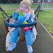 Teddy joined the competition — help win amazing prizes! baby, child, swing, toy, park, grass, hat, blue_clothing, socks, smile, outdoor, playground, fence, chain, toy_caterpillar, happy, cute, infant, warm_clothing, daylight