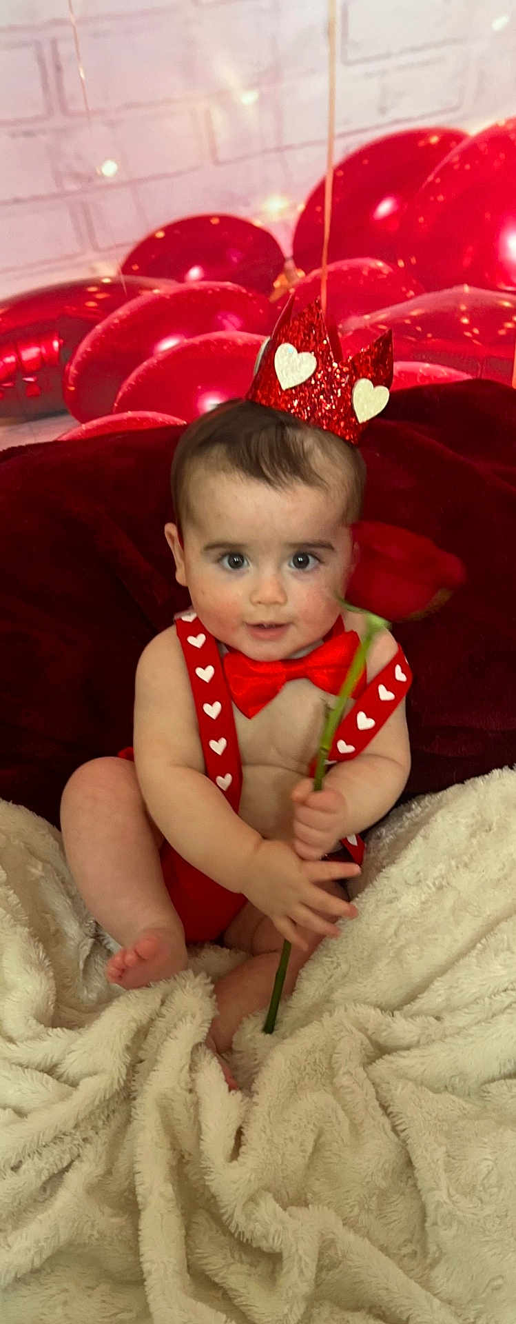 Axton is registered to the contest to win money with this photo: baby, child, red_crown, red_bow_tie, red_suspender, rose, balloons, fluffy_blanket, heart_shapes, indoor, portrait, cute, smiling, celebration, festive, holiday, valentines_day, soft_texture, infant, happy