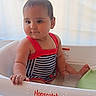 baby, child, bathtub, water, swimsuit, striped_clothing, red_straps, pony_tail, infant, sitting, curious, water_droplets, plastic_tub, indoor, cute, young_child, playtime, relaxed, skin, face