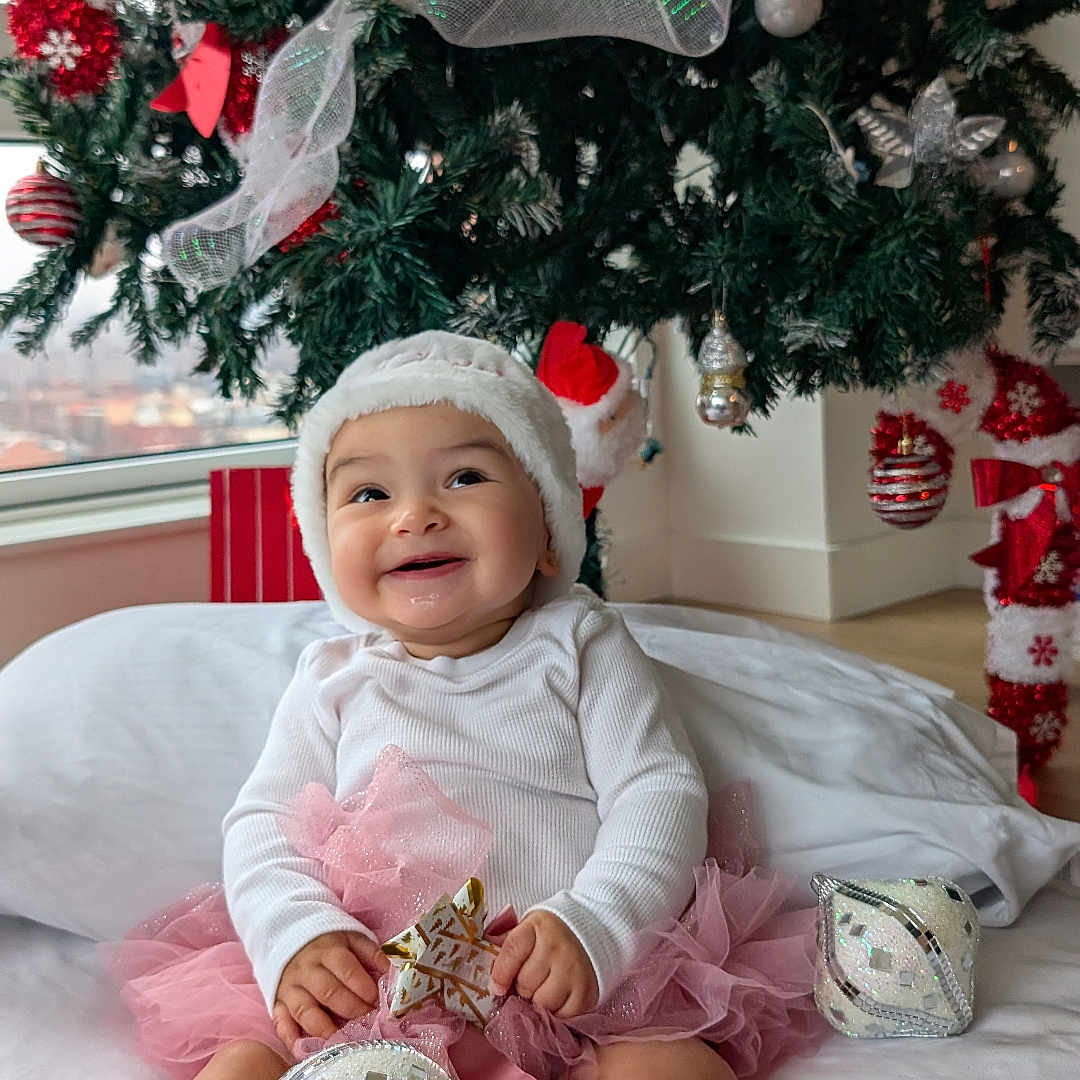 Mirana joined the competition — help win amazing prizes! baby, bauble, bed, christmas_tree, cute, festive, happy, holiday_decor, indoors, infant, ornament, pillow, pink_tutu, pompom_sock, portrait, present, santa_hat, smiling, toy, white_top