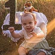Savannah joined the competition — help win amazing prizes! baby, child, grass, outdoor, sunlight, plush_toy, fox, number_one, blanket, smiling, happy, cute, sitting, nature, greenery, warm_light, portrait, soft_clothing, first_birthday, playful