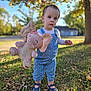 Savannah joined the competition — help win amazing prizes! toddler, child, plush_toy, elephant, overalls, blue_shoes, grass, autumn_leaves, outdoor, sunlight, tree, nature, cute, young_child, portrait, standing, daytime, playful, casual_clothing, person