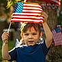 child, boy, american_flag, flag, outdoor, daylight, grass, tree, patriotic, celebration, holiday, summer, casual_clothing, blue_shirt, young, person, nature, holding, festive, portrait