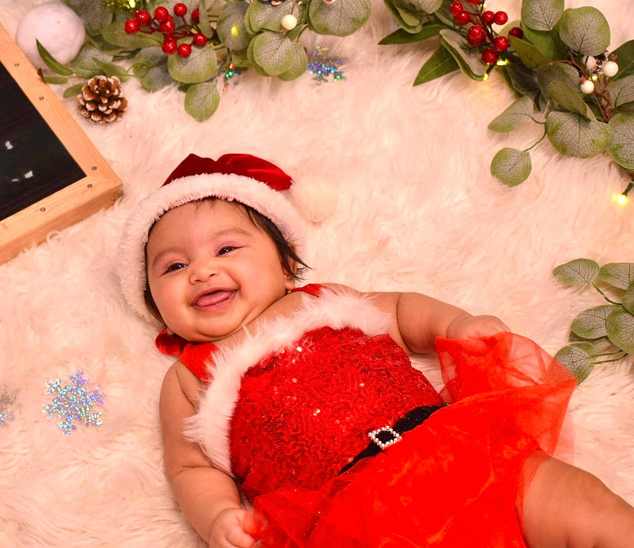 Raavya is registered to the contest to win money with this photo: baby, infant, smiling, christmas_hat, red_dress, holiday, festive, smile, fluffy_rug, pine_cone, greenery, snowflake_decoration, cute, portrait, indoors, celebration, christmas, child, happy, toddler