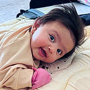 Raavya is registered to the contest to win money with this photo: baby, infant, child, cute, smiling, lying_down, bed, mattress, blanket, mitten, clothing, face, hair, indoor, person, soft, patterned, joyful, curious, cozy